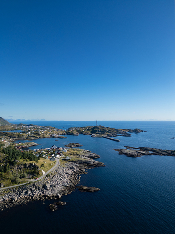 Aerial view of the coastal village of A with traditional houses rocky shores and a winding road along the deep blue sea under a clear sky in A Nordland Norway.