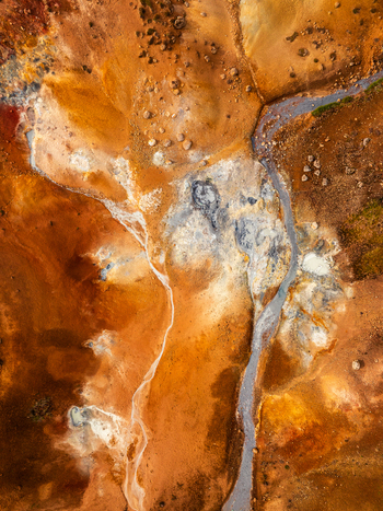 Aerial view of vibrant geothermal landscape with orange and red mineral deposits steaming vents and volcanic soil patterns in Iceland. Aerial view of vibrant geothermal landscape with orange and red mineral deposits steaming vents and volcanic soil patterns in Iceland.