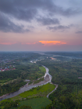 Aerial view of Taba Tembilang river winding through lush greenery and palm oil plantations under a dramatic sunset sky in Arga Makmur Bengkulu Indonesia.