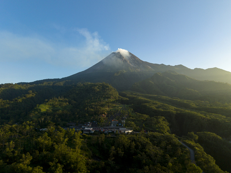 Aerial view of Bunker Kaliadem Merapi and the smoking peak of Mount Merapi surrounded by dense tropical forests in Kecamatan Pakem Daerah Istimewa Yogya Indonesia. Aerial view of Bunker Kaliadem Merapi and the smoking peak of Mount Merapi surrounded by dense tropical forests in Kecamatan Pakem Daerah Istimewa Yogya Indonesia.