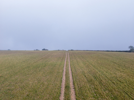 Aerial view of agricultural farmland with tractor tracks cutting through a harvested field under an overcast sky in Looe Cornwall United Kingdom. Aerial view of agricultural farmland with tractor tracks cutting through a harvested field under an overcast sky in Looe Cornwall United Kingdom.