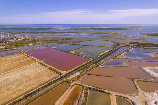 Aerial view of Salinas do Grelha salt pans with vibrant pink brown and green water pools surrounded by coastal wetlands and the Ria Formosa in Olhao Faro Portugal. Aerial view of Salinas do Grelha salt pans with vibrant pink brown and green water pools surrounded by coastal wetlands and the Ria Formosa in Olhao Faro Portugal.