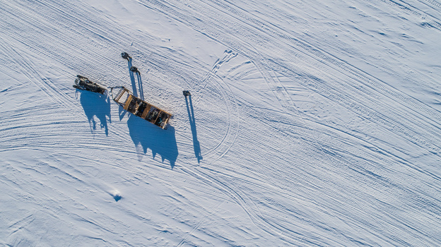 Aerial view of a snowmobile pulling a sled across a vast snow covered landscape with visible tracks and long shadows in Kirkenes Finnmark Norway. Aerial view of a snowmobile pulling a sled across a vast snow covered landscape with visible tracks and long shadows in Kirkenes Finnmark Norway.