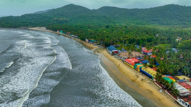 Aerial view of Palolem Beach with its crescent shaped coastline colorful beach shacks lush green hills and waves rolling onto the sand in Canacona Goa India.