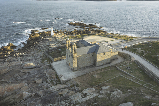 Aerial view of the Sanctuary of Nosa Senora da Barca situated on the rocky coastline near a lighthouse and the Atlantic Ocean in Galicia Spain.