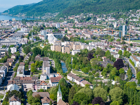 Aerial view of the urban landscape featuring modern residential complexes lush green parks and the Schuss river winding through the city under a clear blue sky Biel Bienne Canton of Bern Switzerland.