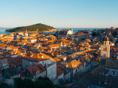 View of Dubrovnik Old Town with iconic orange rooftops a bell tower and Lokrum Island in the distance under a clear blue sky in Dubrovnik Dubrovnik Neretva County Croatia. View of Dubrovnik Old Town with iconic orange rooftops a bell tower and Lokrum Island in the distance under a clear blue sky in Dubrovnik Dubrovnik Neretva County Croatia.