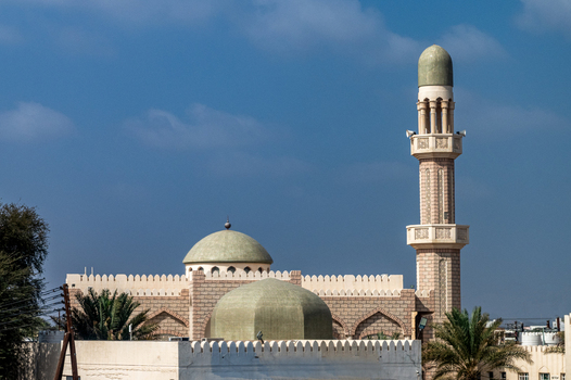 View of a traditional mosque with domes and a tall minaret under a clear blue sky in Muscat Muscat Governorate Oman. View of a traditional mosque with domes and a tall minaret under a clear blue sky in Muscat Muscat Governorate Oman.