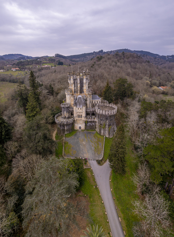 Aerial view of Butron Castle surrounded by dense forest and rolling hills under a cloudy sky in Butroi Euskadi Spain. Aerial view of Butron Castle surrounded by dense forest and rolling hills under a cloudy sky in Butroi Euskadi Spain.