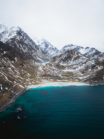 Aerial view of turquoise waters meeting snow dusted mountains a serene contrast of warmth and chill at Haukland Beach Leknes Nordland Norway. Aerial view of turquoise waters meeting snow dusted mountains a serene contrast of warmth and chill at Haukland Beach Leknes Nordland Norway.
