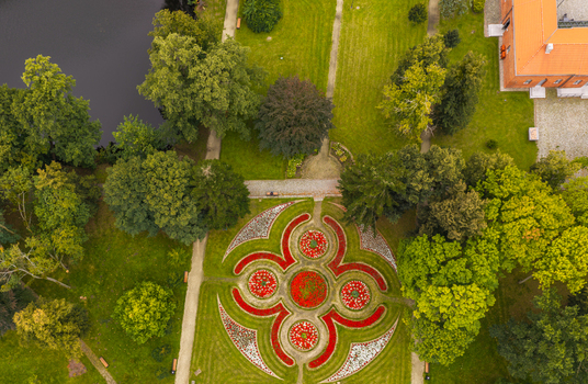 Aerial view of a geometric flower bed in the park of the Bishops Palace surrounded by lush trees a pond and a brick building in Pelplin Pomeranian Voivodeshi Poland. Aerial view of a geometric flower bed in the park of the Bishops Palace surrounded by lush trees a pond and a brick building in Pelplin Pomeranian Voivodeshi Poland.