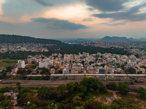 Aerial view of the urban landscape of Udaipur with railway tracks dense trees and distant hills under a dramatic sunset sky in Udaipur Rajasthan India. Aerial view of the urban landscape of Udaipur with railway tracks dense trees and distant hills under a dramatic sunset sky in Udaipur Rajasthan India.