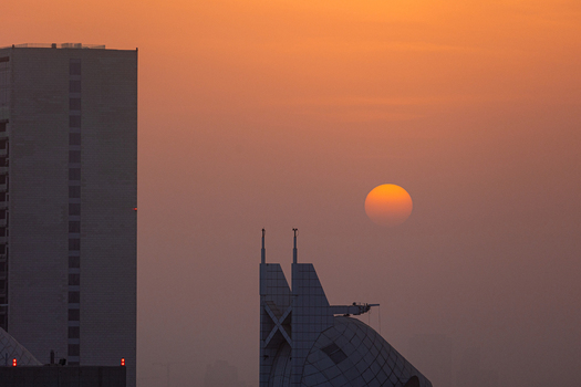 View of the sun setting behind modern skyscrapers and architectural structures under a hazy orange sky Dubai Dubai United Arab Emirates. View of the sun setting behind modern skyscrapers and architectural structures under a hazy orange sky Dubai Dubai United Arab Emirates.