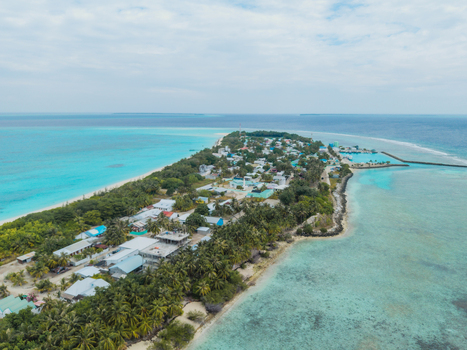 Aerial view of turquoise waters embracing the crescent shaped island with its vibrant greenery and clustered buildings Vashafaru Island Thiladhummathi Atoll Maldives. Aerial view of turquoise waters embracing the crescent shaped island with its vibrant greenery and clustered buildings Vashafaru Island Thiladhummathi Atoll Maldives.