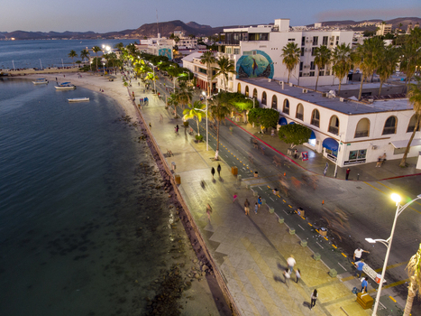 Aerial view of the Malecon de La Paz at dusk featuring palm trees streetlights people walking along the waterfront and coastal buildings in La Paz Baja California Sur Mexico.