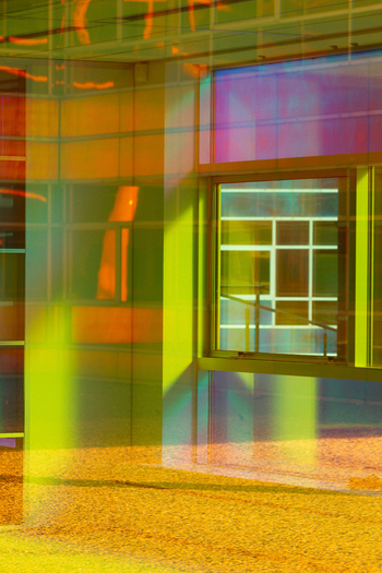 View of vibrant yellow and green glass panels create a kaleidoscopic facade with a window reflecting light casting shadows on the ground Almere Flevoland Netherlands. View of vibrant yellow and green glass panels create a kaleidoscopic facade with a window reflecting light casting shadows on the ground Almere Flevoland Netherlands.