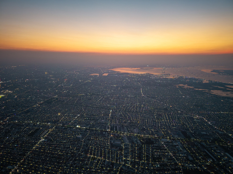 Aerial view of the sprawling city at sunset with urban lights glowing across the dense residential grid and the coastline Surabaya East Java Indonesia.