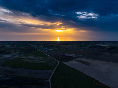 Aerial view of the sunset over the Baltic Sea with golden light reflecting on the water dark clouds and agricultural fields in Skatre South Kurzeme Municip Latvia. Aerial view of the sunset over the Baltic Sea with golden light reflecting on the water dark clouds and agricultural fields in Skatre South Kurzeme Municip Latvia.