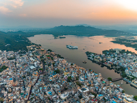 Aerial view of Lake Pichola and the historic city of Udaipur with dense urban architecture the iconic Lake Palace and surrounding hills at sunset in Udaipur Rajasthan India.