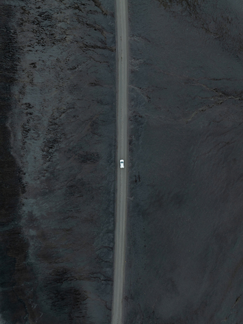 Aerial view of a white car driving along a straight road through a vast dark volcanic landscape Iceland. Aerial view of a white car driving along a straight road through a vast dark volcanic landscape Iceland.