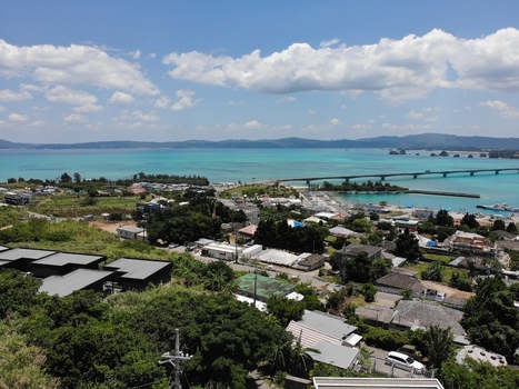 Aerial view of Kouri Bridge stretching across the turquoise ocean toward Yagaji Island with lush greenery and residential buildings in Nakijin Okinawa Japan. Aerial view of Kouri Bridge stretching across the turquoise ocean toward Yagaji Island with lush greenery and residential buildings in Nakijin Okinawa Japan.