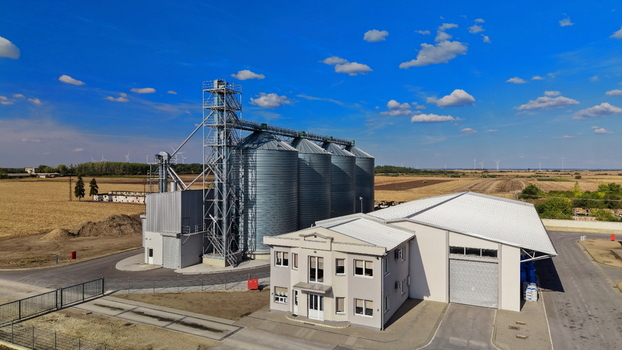 Aerial view of the storage silo facility with large metal grain silos and an adjacent industrial building set against a flat agricultural landscape in Bavaniste Vojvodina Serbia.