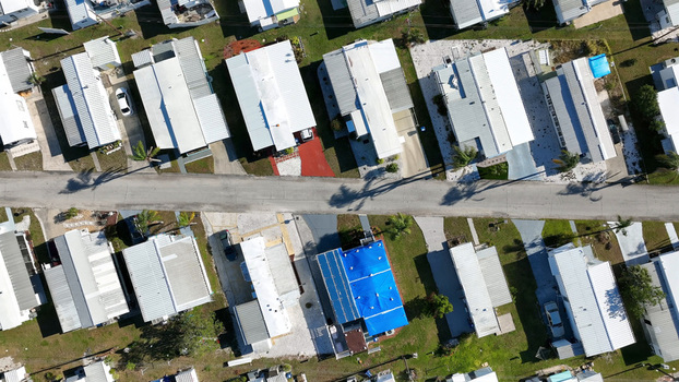 Aerial view of a residential neighborhood with rows of mobile homes a paved road and a house with a blue tarp on the roof in Bradenton Florida United States.