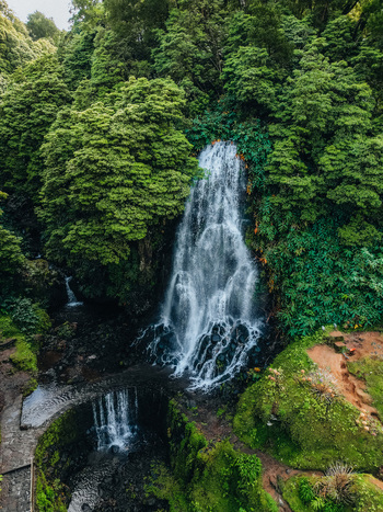 Aerial view of cascading waterfall plunges amidst verdant foliage reflecting in a serene pool at its base Achada Açores Portugal. Aerial view of cascading waterfall plunges amidst verdant foliage reflecting in a serene pool at its base Achada Açores Portugal.