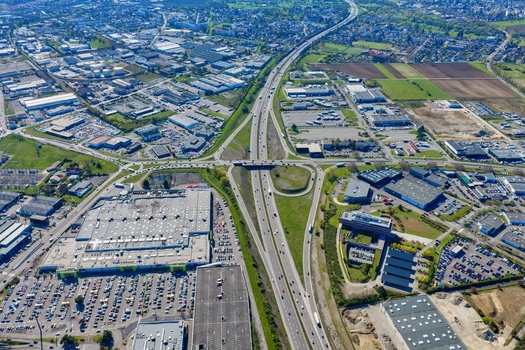 Aerial view of a highway cutting through a city surrounded by industrial buildings and green fields creating a stark contrast between urban development and nature Sausheim Grand Est France.