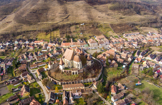 Aerial view of the Biertan Fortified Church surrounded by historic village houses with red tiled rooftops and rolling hills in Biertan Sibiu Romania.