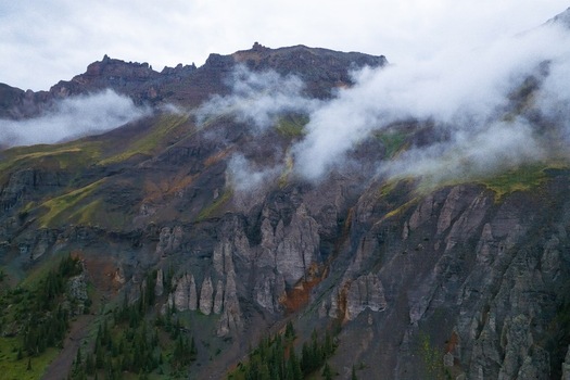 Aerial view of Mt. Sneffels in Yankee Boy Basin featuring dramatic rock formations patches of green alpine vegetation and low hanging clouds in Ouray Colorado United States.