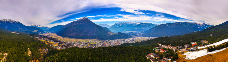 Aerial view of the town of Imst nestled in a valley surrounded by dense evergreen forests and majestic snow capped Alpine peaks under a bright blue sky Imst Tyrol Austria. Aerial view of the town of Imst nestled in a valley surrounded by dense evergreen forests and majestic snow capped Alpine peaks under a bright blue sky Imst Tyrol Austria.