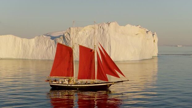 Aerial view of a sailboat with red sails near an iceberg Greenland. Aerial view of a sailboat with red sails near an iceberg Greenland.
