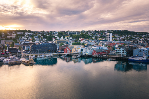 Aerial view of Tromso harbor at sunset with colorful wooden buildings modern architecture and boats docked in the calm water in Tromso Troms Norway.