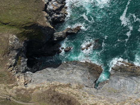 Aerial view of The Rumps showing rugged coastal cliffs dark rock formations and turquoise sea water with white waves crashing against the shore in Wadebridge England United Kingdom. Aerial view of The Rumps showing rugged coastal cliffs dark rock formations and turquoise sea water with white waves crashing against the shore in Wadebridge England United Kingdom.