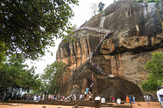 Sri Lanka 21 February 2026 View of the Lion s Paw entrance at Sigiriya rock fortress with tourists climbing the steep metal staircase against the massive granite cliff.