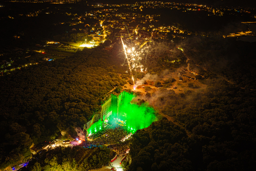 Aerial view of a nighttime music festival held in a quarry with vibrant green stage lighting pyrotechnics and a crowd of people gathered in Vintijan Istria County Croatia. Aerial view of a nighttime music festival held in a quarry with vibrant green stage lighting pyrotechnics and a crowd of people gathered in Vintijan Istria County Croatia.