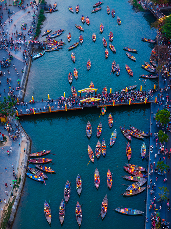 Aerial view of traditional wooden boats floating on the river with glowing lanterns and people walking on the bridge in Vietnam. Aerial view of traditional wooden boats floating on the river with glowing lanterns and people walking on the bridge in Vietnam.