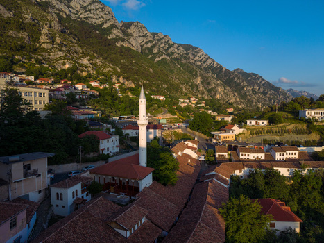 Aerial view of the Murad Bey Mosque minaret and the historic red tiled rooftops of the Old Bazaar nestled against the rocky slopes of Mount Kruje in Kruje Durres County Albania.