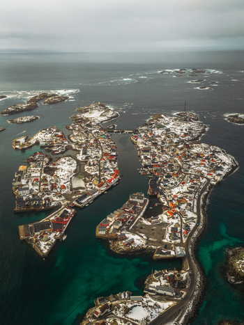 Aerial view of snow dusted rooftops and harbors create a striking contrast against the dark shimmering waters surrounding the island Henningsv&aelig;r Nordland Norway.