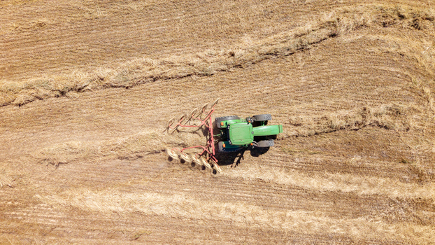Aerial view of a green tractor pulling a hay rake across a dry harvested field in Philadelphia Western Cape South Africa. Aerial view of a green tractor pulling a hay rake across a dry harvested field in Philadelphia Western Cape South Africa.