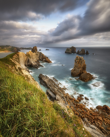 View of dramatic jagged rock formations and steep cliffs along the rugged coastline under a moody cloudy sky Asturias Asturias Spain. View of dramatic jagged rock formations and steep cliffs along the rugged coastline under a moody cloudy sky Asturias Asturias Spain.