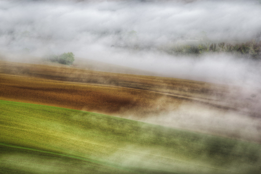 Aerial view of rolling hills with green and brown fields partially obscured by thick morning mist in the countryside of Corridonia Marche Italy. Aerial view of rolling hills with green and brown fields partially obscured by thick morning mist in the countryside of Corridonia Marche Italy.