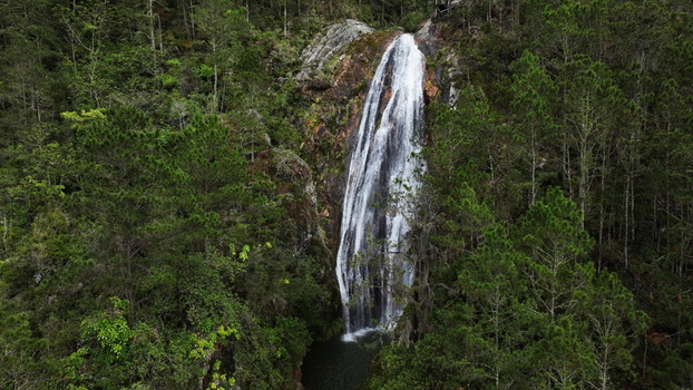 Aerial view of Salto de Aguas Blancas waterfall cascading down a rocky cliff surrounded by dense pine forest in Constanza La Vega Province Dominican Republic. Aerial view of Salto de Aguas Blancas waterfall cascading down a rocky cliff surrounded by dense pine forest in Constanza La Vega Province Dominican Republic.