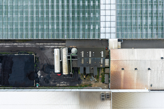 Aerial view of production scale greenhouse with large glass panels industrial storage tanks and metal roof structures in Poland.