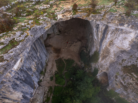 Aerial view of Prohodna Cave with its massive limestone arch rocky cliffs lush greenery and natural light filtering through the cave openings in Karlukovo Lovech Bulgaria. Aerial view of Prohodna Cave with its massive limestone arch rocky cliffs lush greenery and natural light filtering through the cave openings in Karlukovo Lovech Bulgaria.