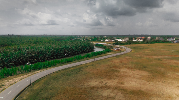 Aerial view of a winding road passing through a landscape with dense palm trees and a small settlement under a cloudy sky in Rivers Nigeria.