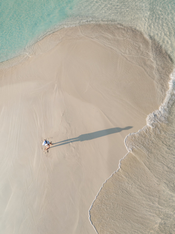 Aerial view of a solitary figure casting a long shadow on the pristine white sands where the turquoise sea gently kisses the shore Dhidhdhoo Maldives.