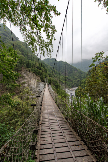 View of the suspension bridge at Taroko National Park surrounded by lush green mountains and a river flowing through the valley in Xiulin Township Hualien County Taiwan.
