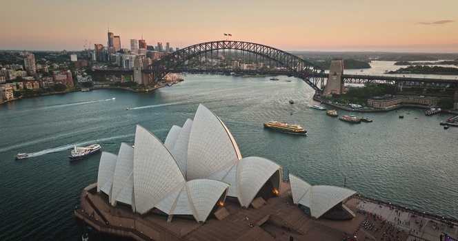 Aerial view of the iconic Sydney Opera House and Sydney Harbour Bridge at sunset with boats in the harbour and city skyline in the background in Sydney New South Wales Australia. Aerial view of the iconic Sydney Opera House and Sydney Harbour Bridge at sunset with boats in the harbour and city skyline in the background in Sydney New South Wales Australia.